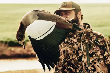 Hunter in camoflage holding a duck that he shot