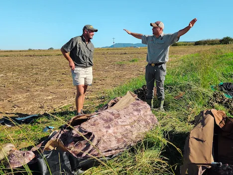 Two hunters talking about their hunt with arms stretched wide immitating a flying bird